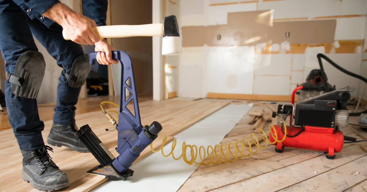 A man working on installing new wooden floors using a heavy-duty staple gun in an under-construction home.