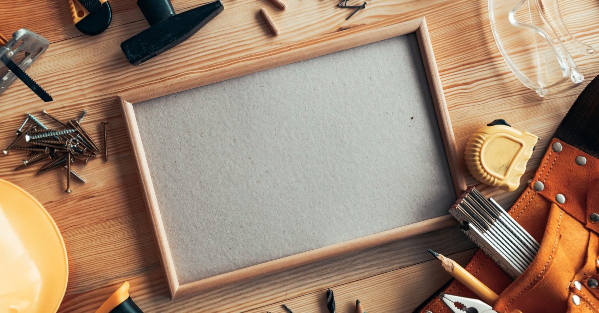 A wooden surface with various tools, including a hammer, nails, drill bits, measuring tape, and safety goggles.