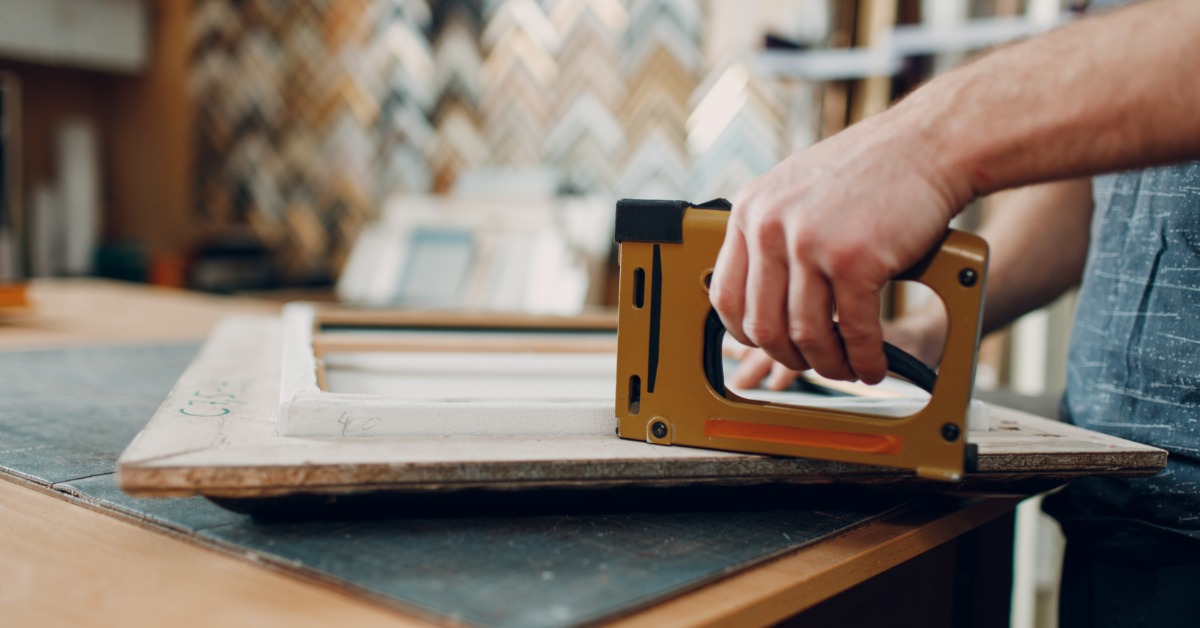 A view inside a picture frame workshop, showing tools, workstations, and an artwork in progress of getting framed.