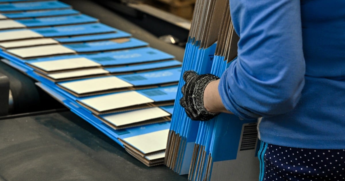 Carpenter assembling furniture uses a stapler to attach fabric to a wooden frame on a workbench in a workshop.