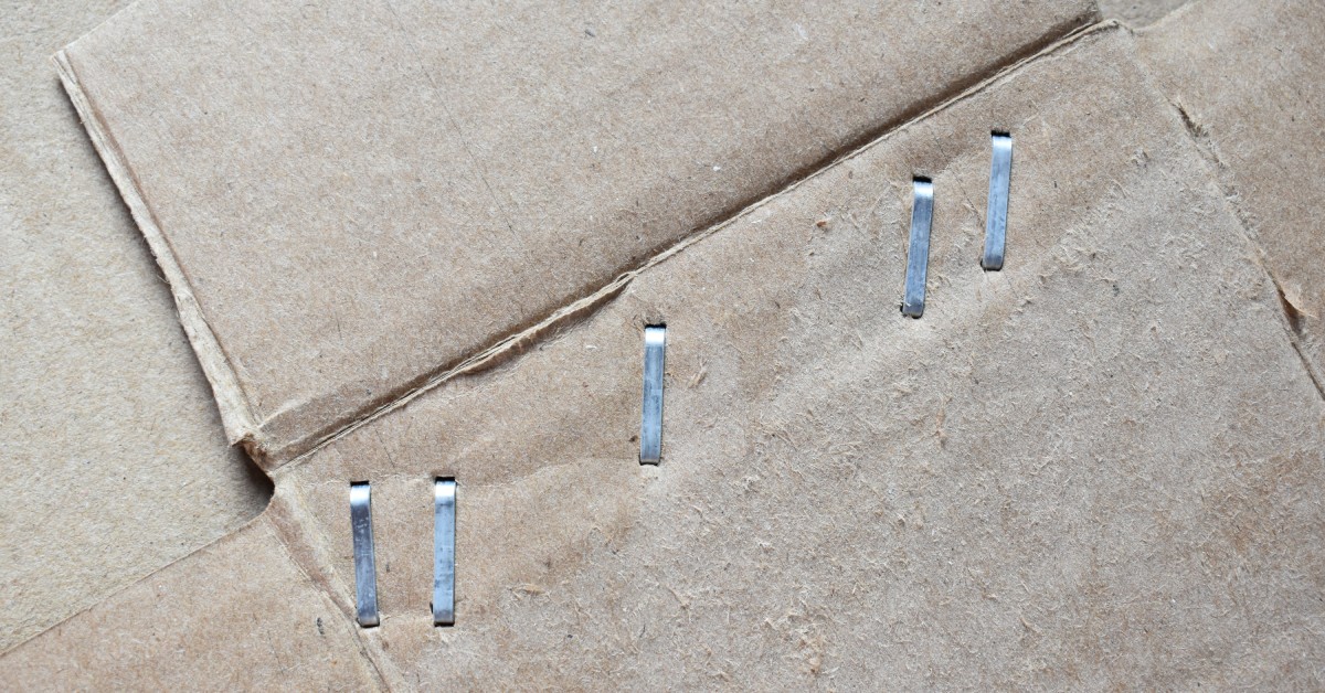 A close-up of a cardboard box with six durable, metal staples driven near the flap that are evenly spaced.