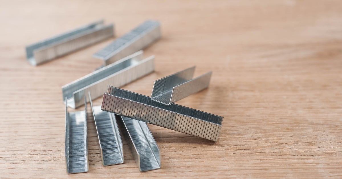 The light reflects off multiple stacks of staples stacked on top of each other, sitting on a wooden table.