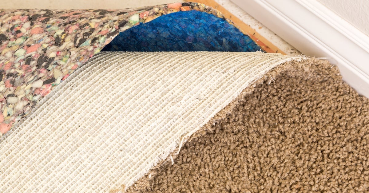 Pulled-back carpet reveals foam padding and bare subfloor in a home room during a flooring installation.
