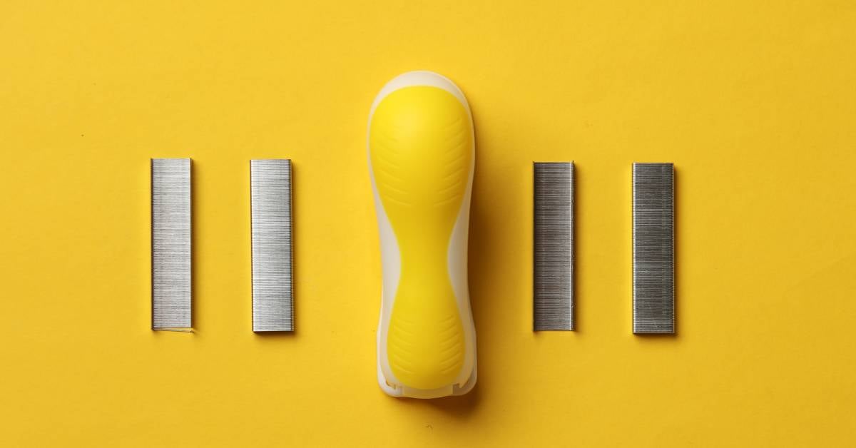 A yellow, rounded stapler with two strips of staples on its left and two strips on its right. The background is also yellow.